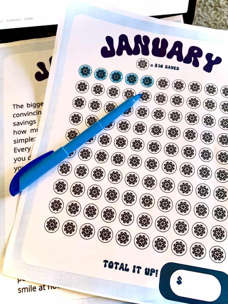 January savings worksheet with a light blue border and white center with several rows of circles with snowflakes inside. 5 snowflakes are colored in blue with a blue highlighter. The blue highlighter is on top of the page. On the bottom right hand corner there is a dark blue box with a white center, to the left there is dark blue text that reads "total it up!"