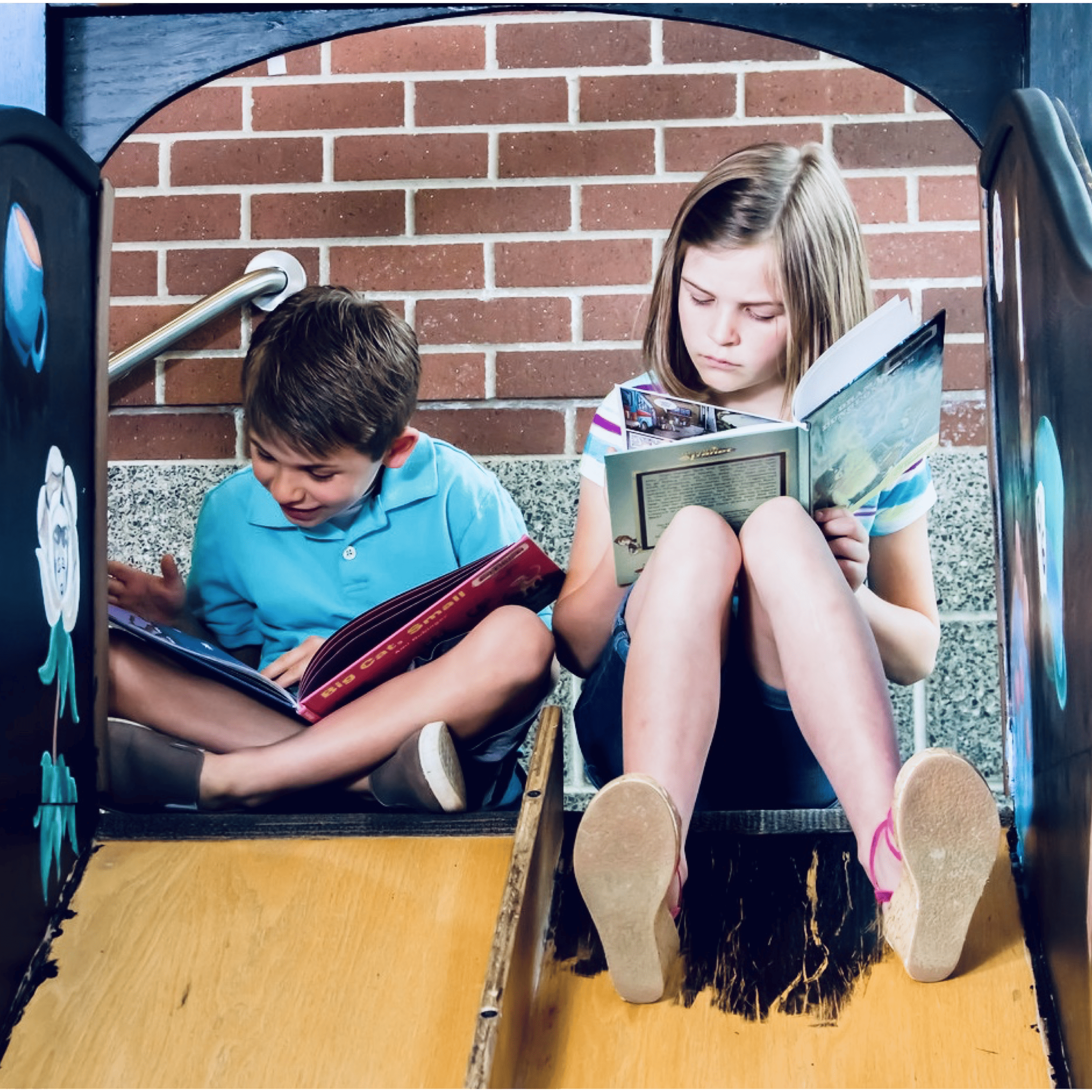 A boy and girl reading books at the top of a double slide