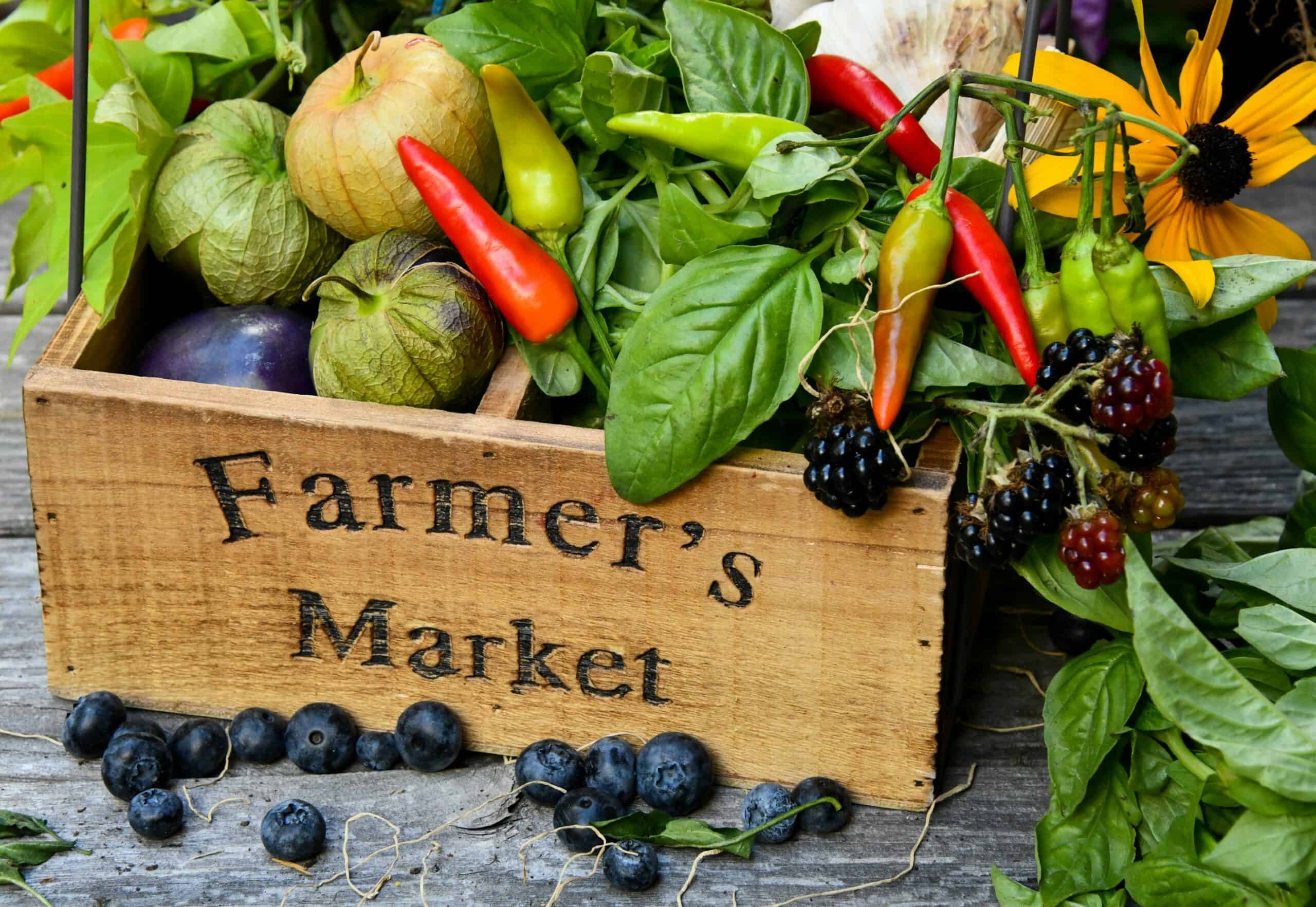 Wooden box of fruits, vegetables, and flowers with black text that reads "Farmer's Market"