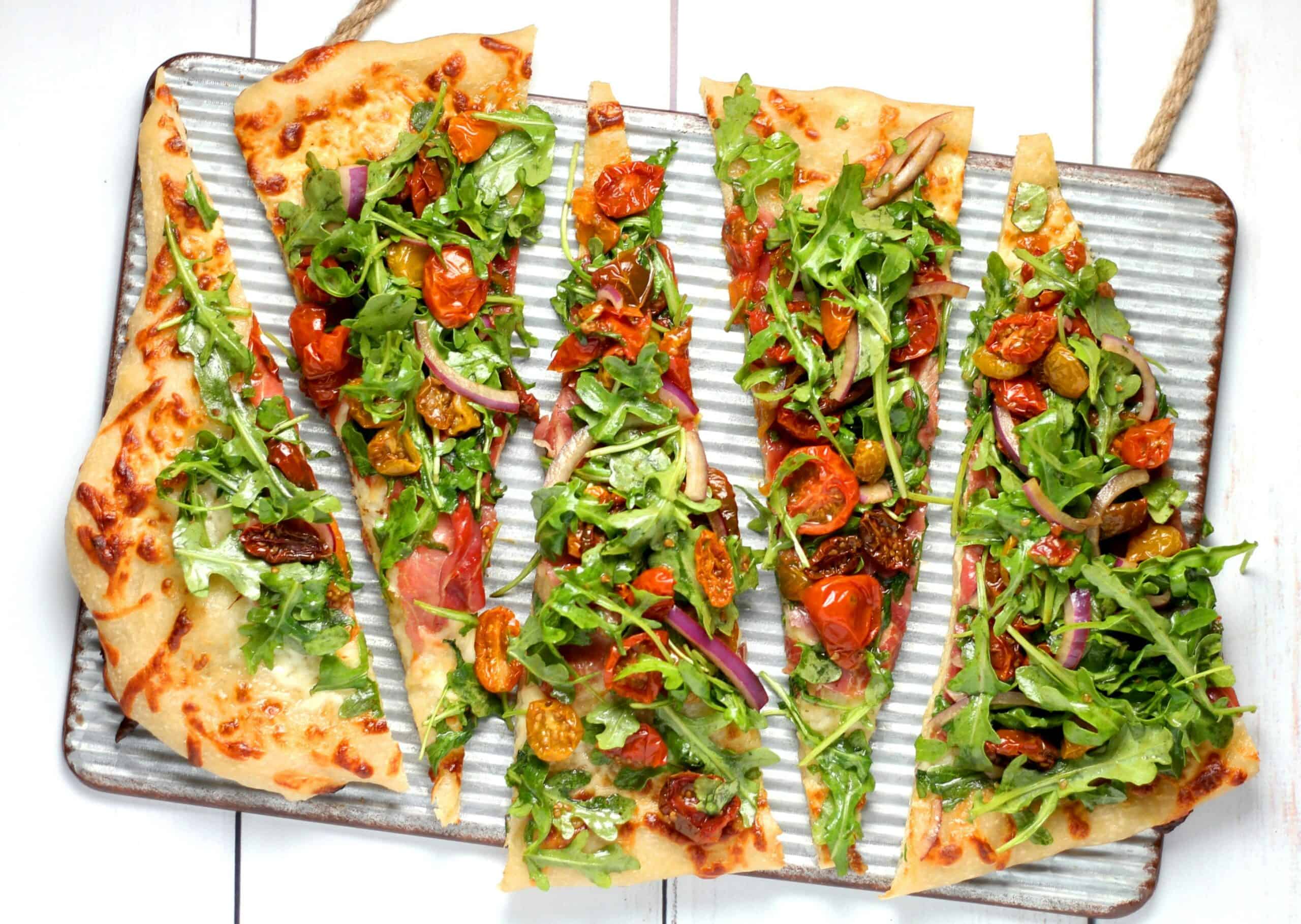 Five slices of a vegan pizza with lots of vegetables on a metal tray
